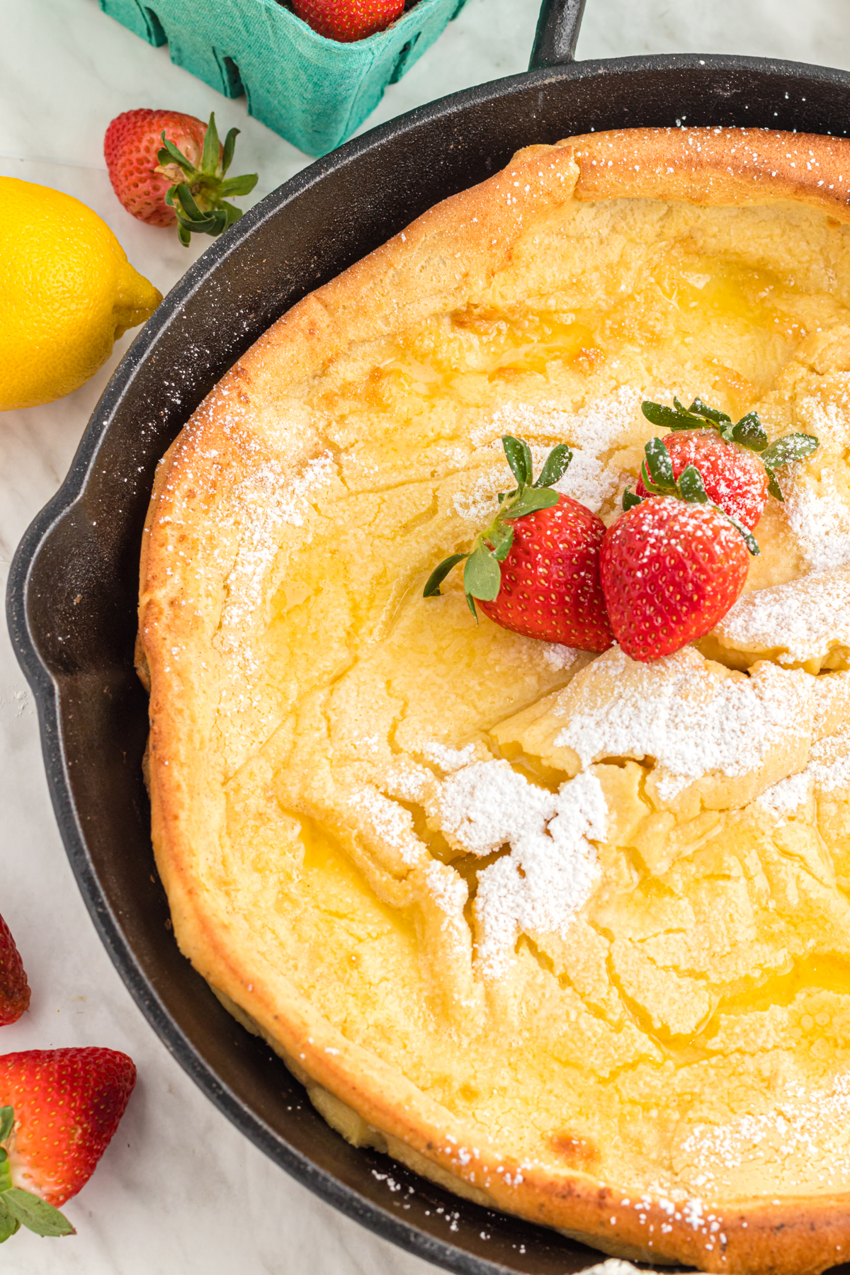 Dutch baby in cast iron pan with strawberries and confectioners sugar.