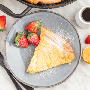 dutch baby slice on plate with strawberries.