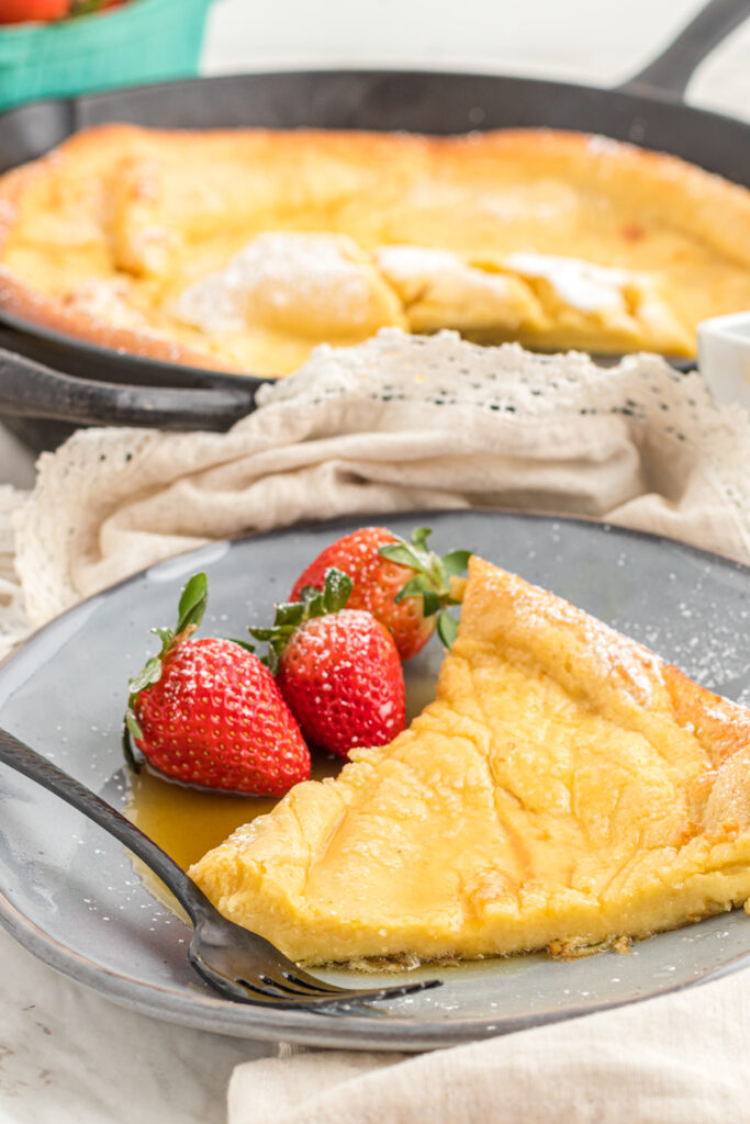 Dutch baby slice on plate with strawberries.