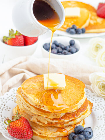 maple syrup being poured on a stack of buttermilk pancakes.