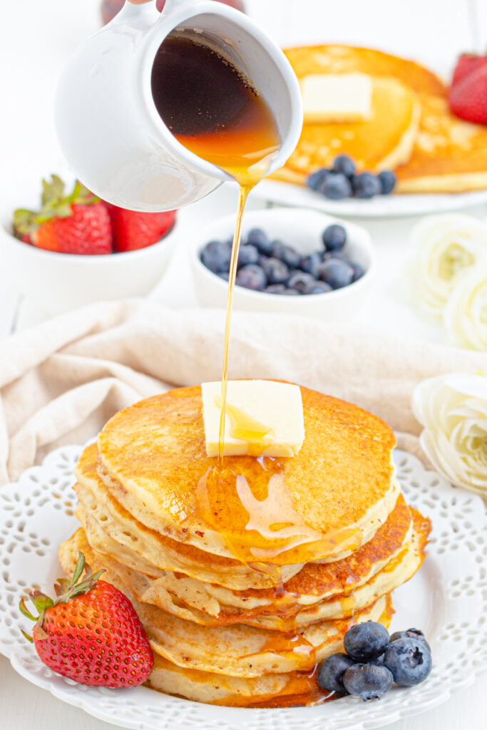 maple syrup being pored on a stack of buttermilk pancakes.
