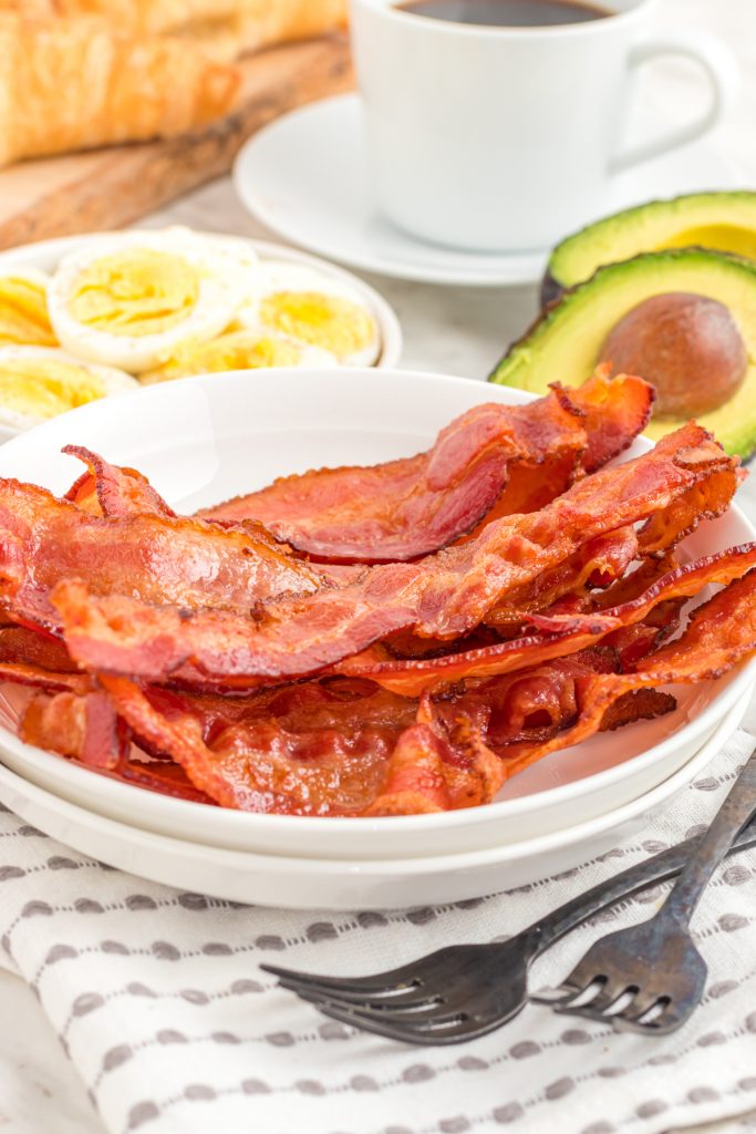 Bacon cooked in the air fryer on a plate, with eggs and avocados on side plates