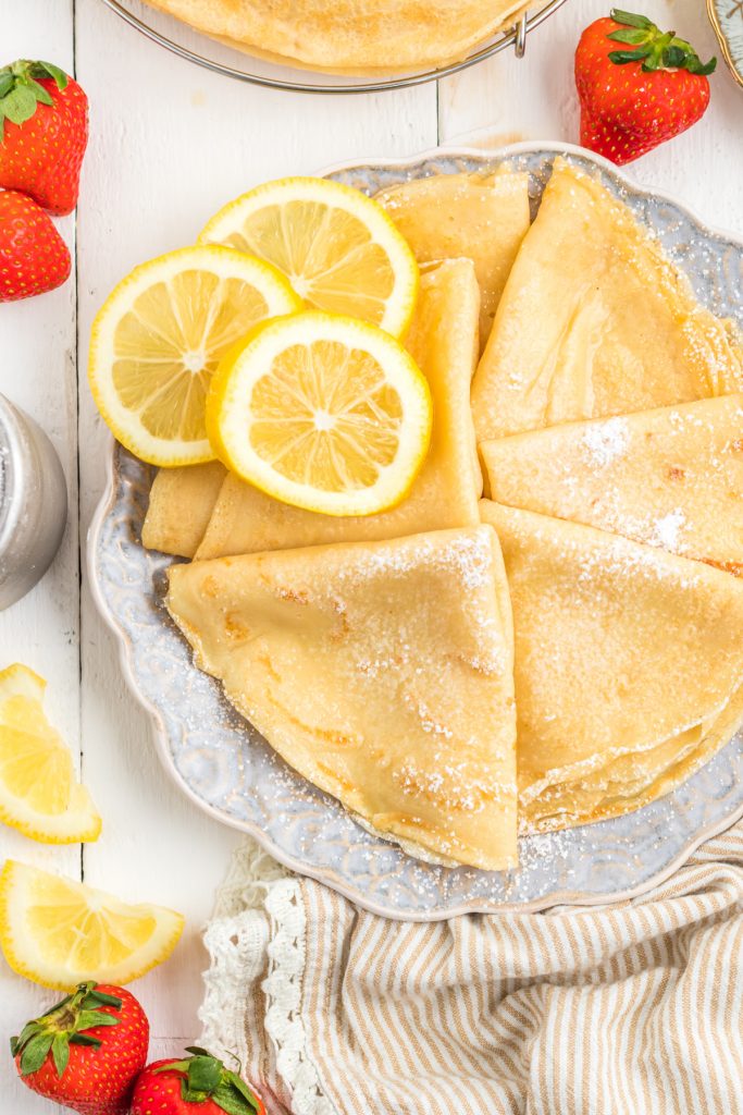 Parisian Crêpes  on a plate with lemon slices and strawberries on the table.