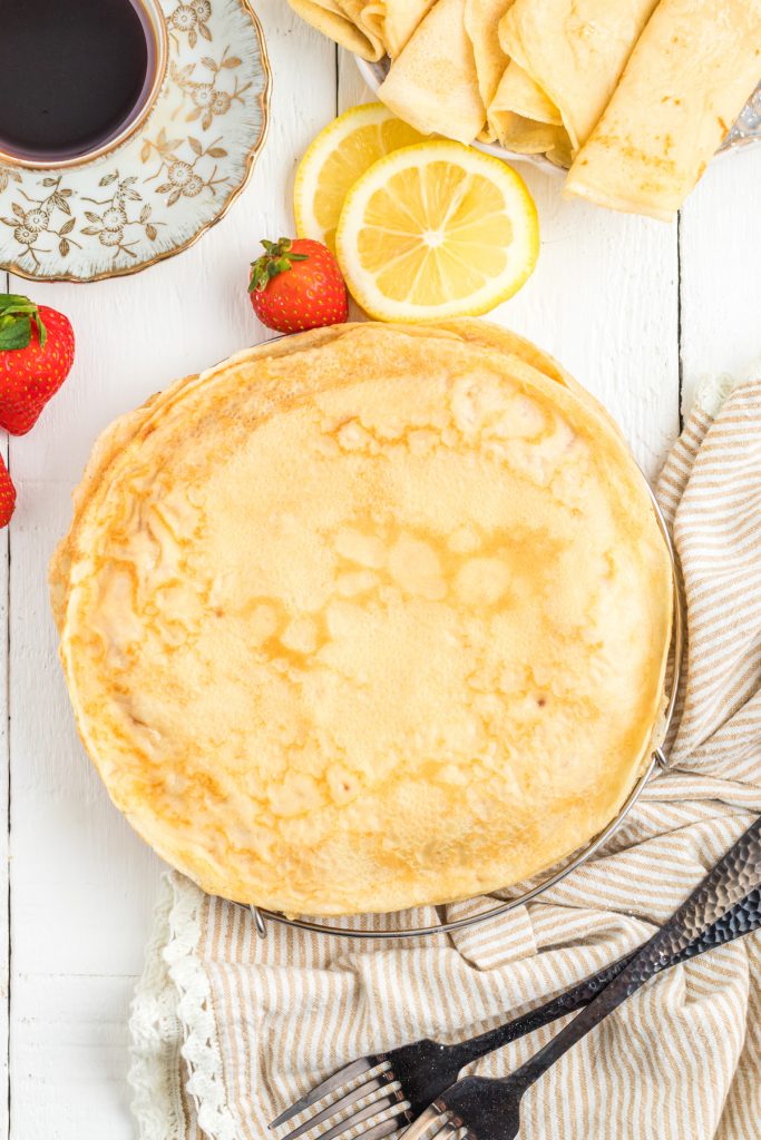 Parisian Crêpes stacked on table with cutlery lemon slices and strawberries.