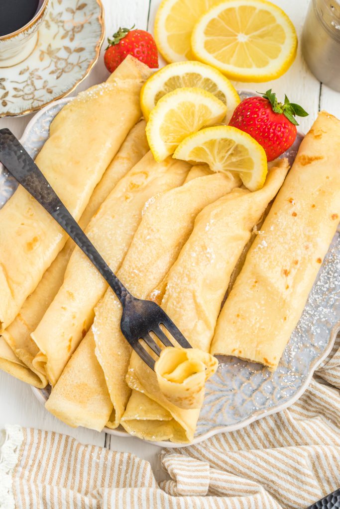 Rolled crepes on a plate with strawberries and lemon