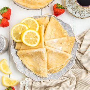crepes folded in triangles in a plate with strawberries , lemon slices and espresso.