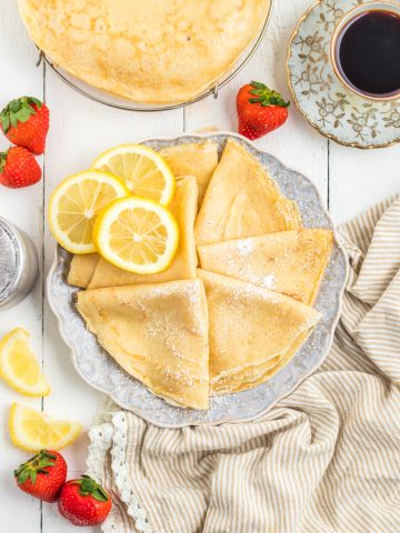 crepes folded in triangles in a plate with strawberries , lemon slices and espresso.