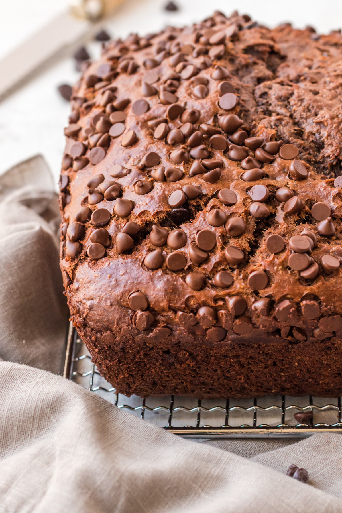 Chocolate banana bread on a cooling rack, covered with chocolate chips.