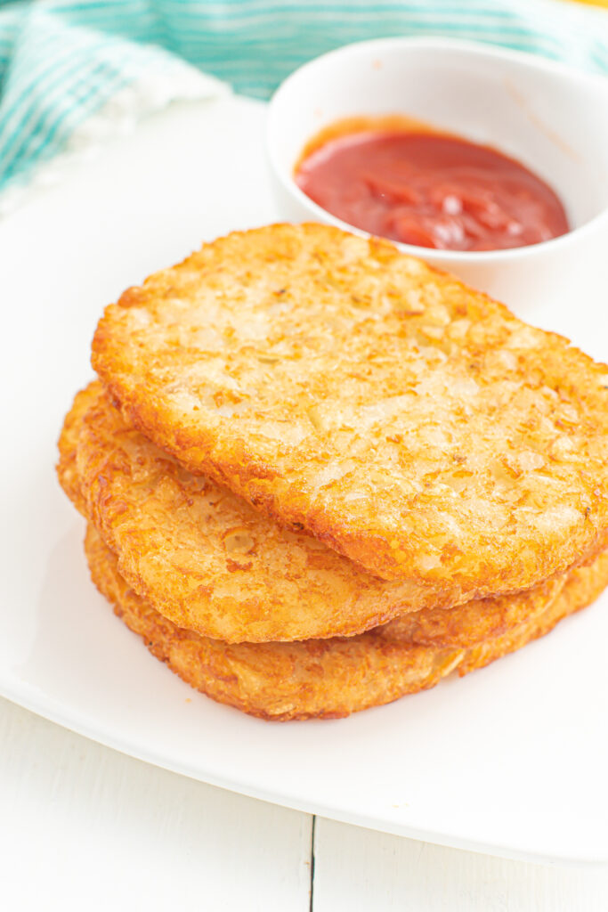 air fryer hashbrowns stacked on a plate with a bowl of ketchup.