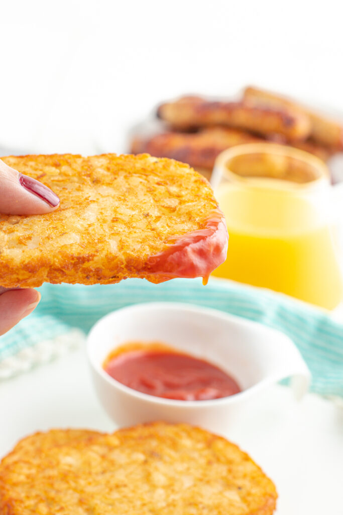 Hash brown patty being dipped in ketchup.