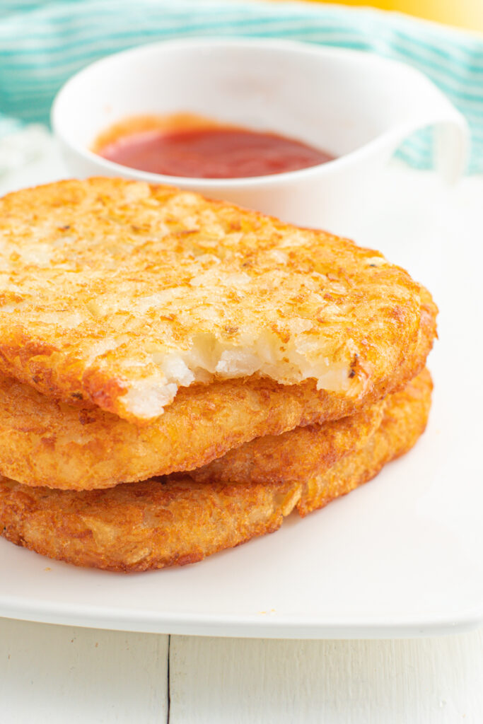 Stack of hash browns on a plate with a bite out of one.