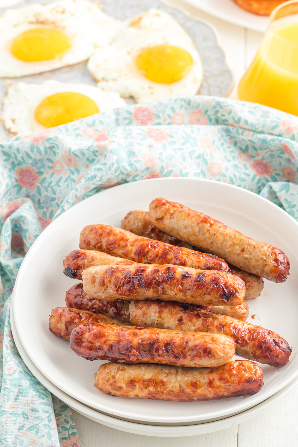 Sausages on a plate on table with eggs and juice.