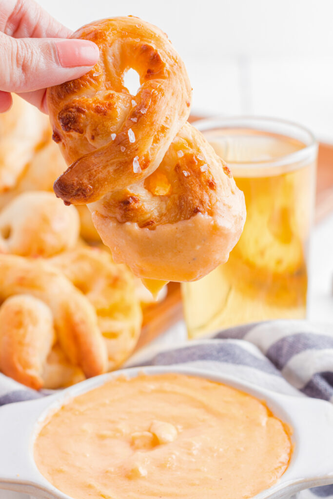 Pretzel being held with cheese dip on the edge.