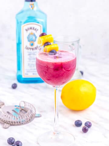 blueberry gin sour cocktail on table with lemon and blueberries.