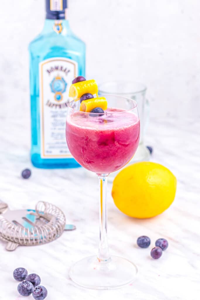 blueberry gin sour on table with lemon and blueberries.