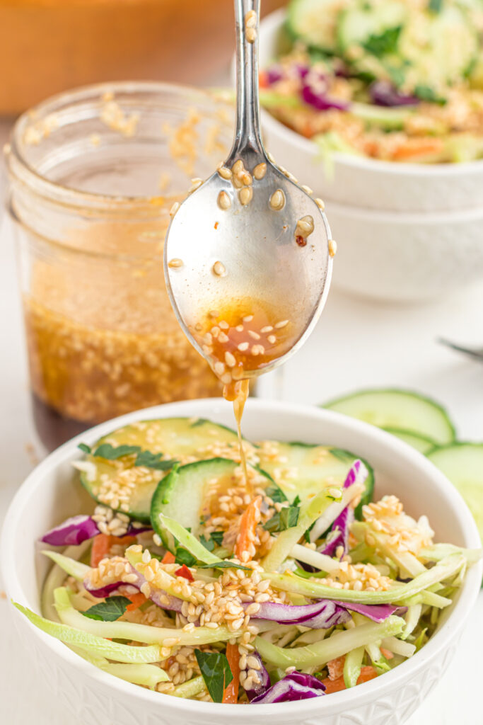 sesame ginger dressing being drizzled from a spoon over salad.