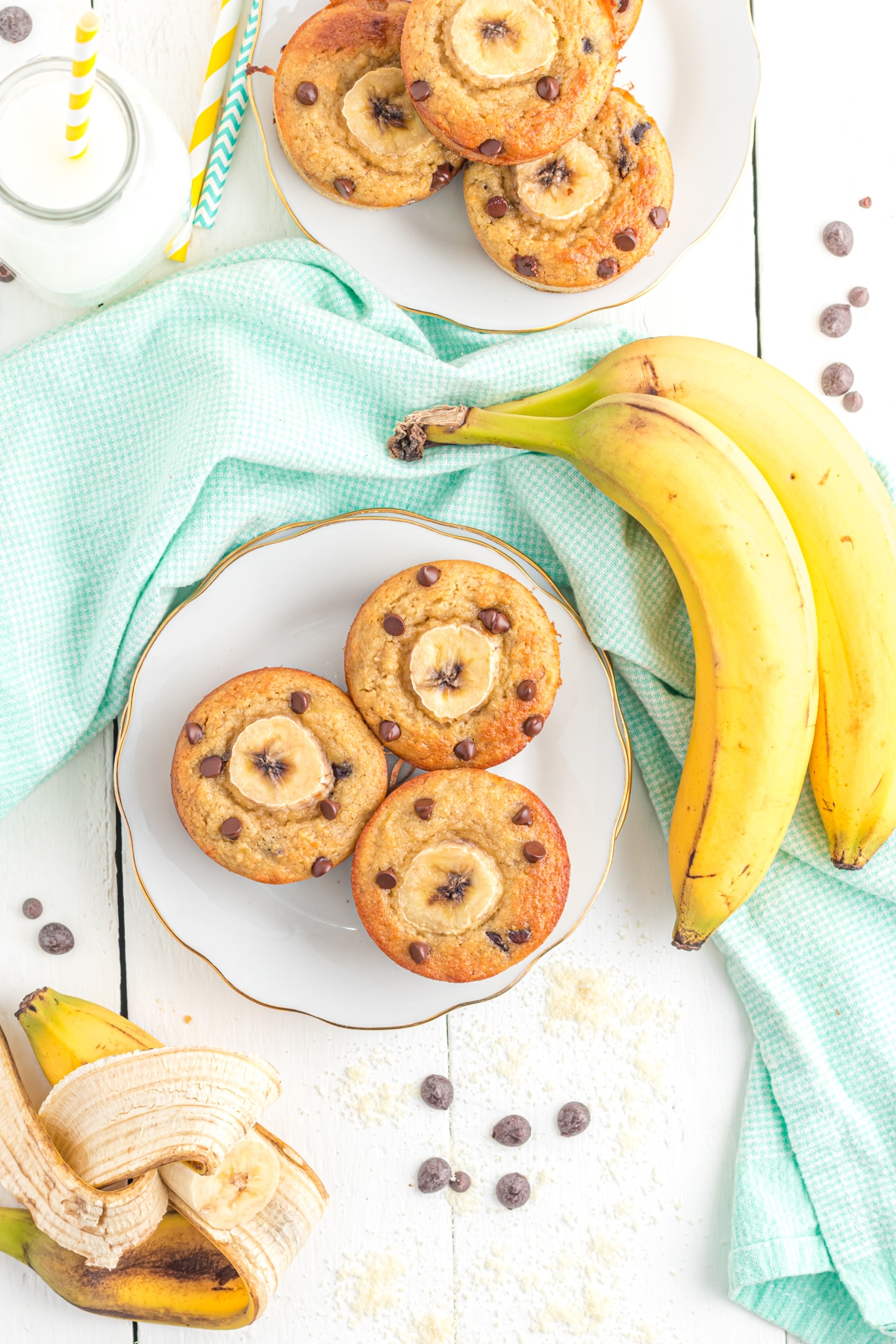 Plates of banana chocolate chip muffins on a plate with bananas and chocolate chips sprinkled around.