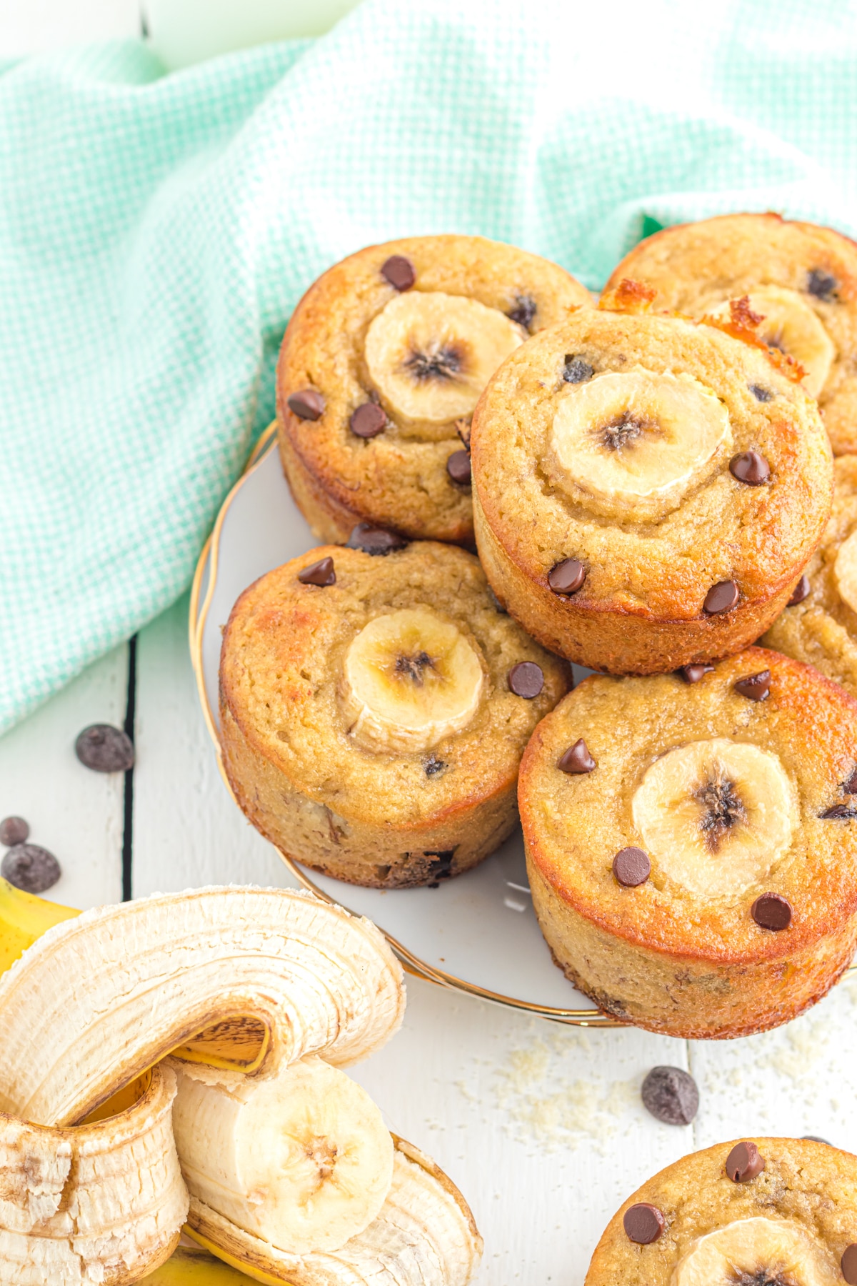 Banana muffins on a plate on a table with a banana and chocolate chips.