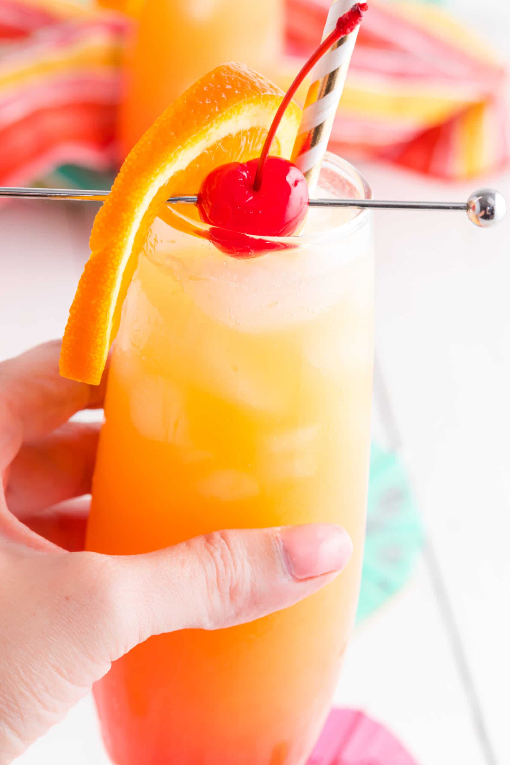Hand holding a orange juice cocktail with fruit garnish.