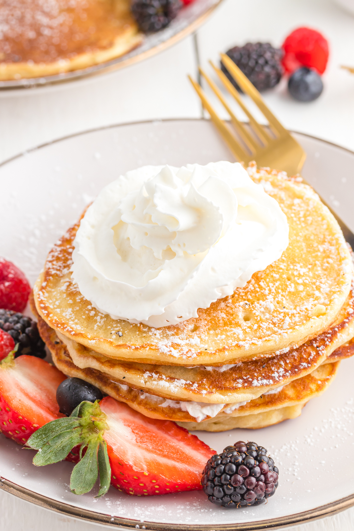 Pancakes dusted with powdered sugar and whipped cream on a plate with berries.