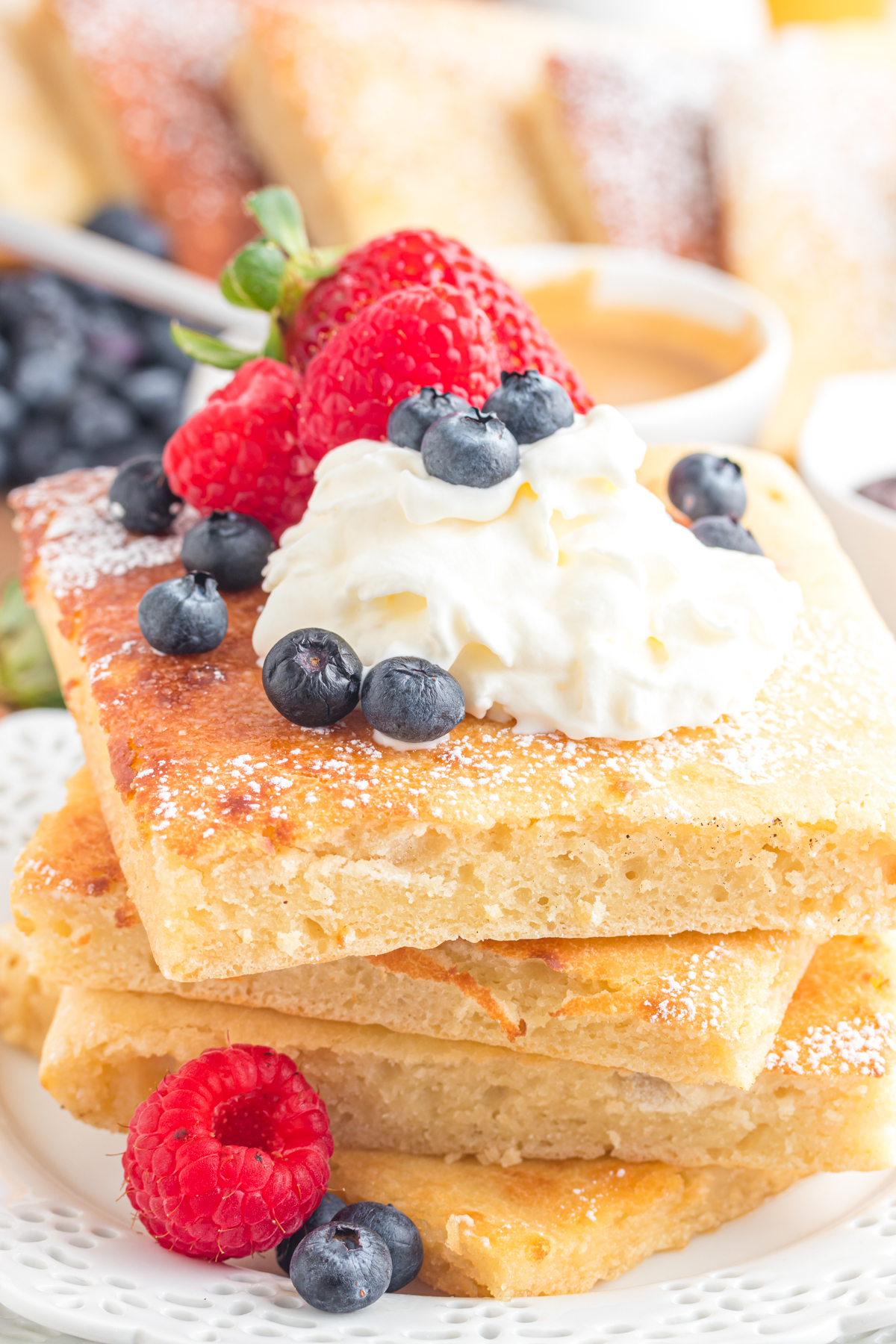 Stack of pancakes on a plate with berries and whipped cream.