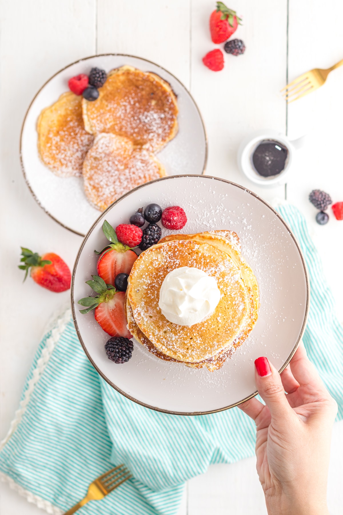 Hand holding plate of pancakes with berries.