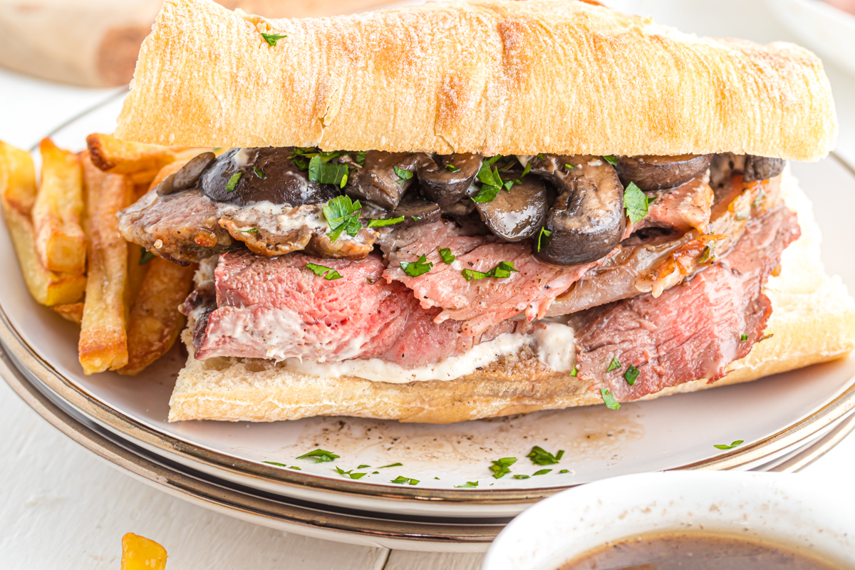 Roast beef on a baguette on a plate with fries.
