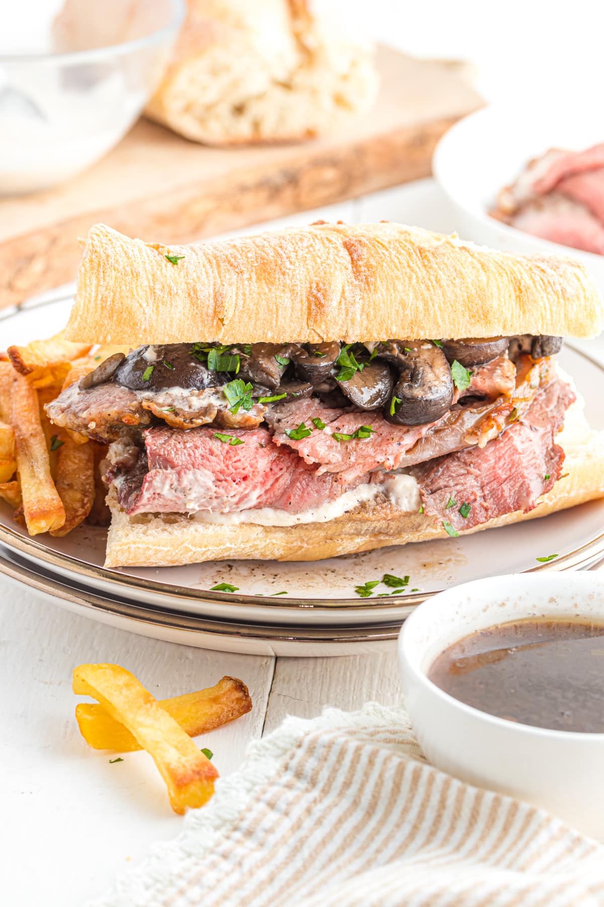 Prime rib sandwich on a plate with fries and  au jus on the side.