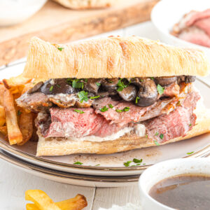 Prime rib sandwich with mushrooms on a plate with fries.
