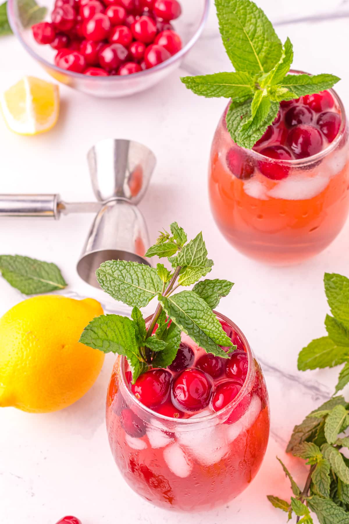Two cranberry cocktails on table with lemon and mint.