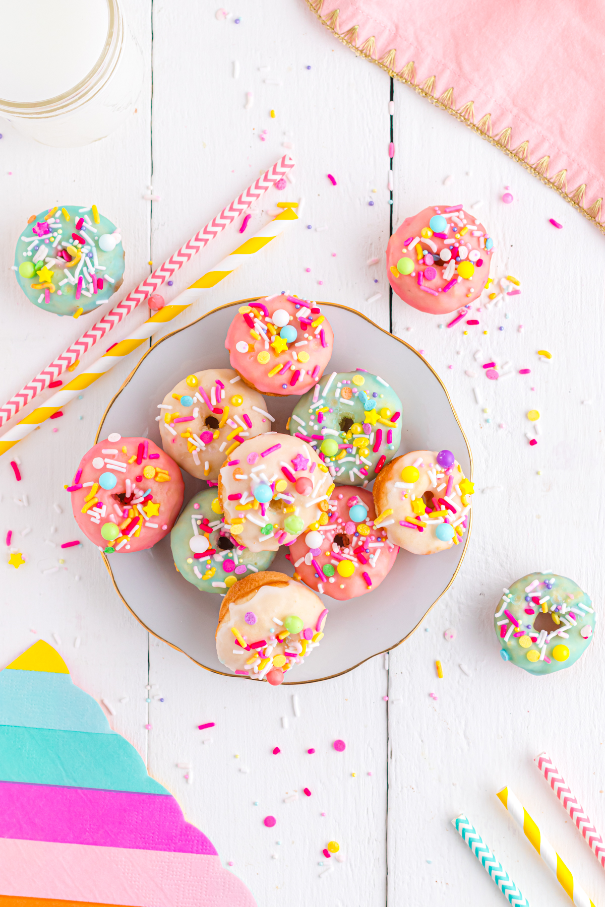 Donuts on a table with sprinkles and straws.