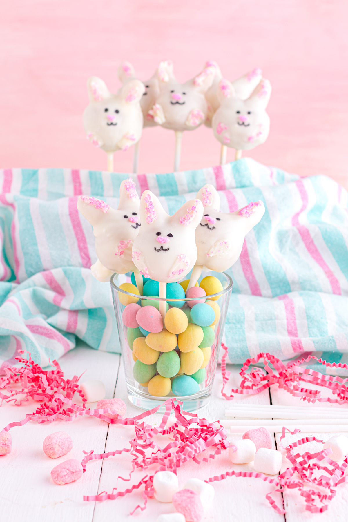 Bunny cake pops on a table with basket stuffing.