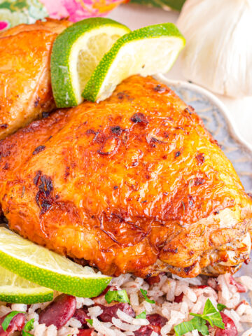 Close up of jerk chicken on a plate surrounded by lime.