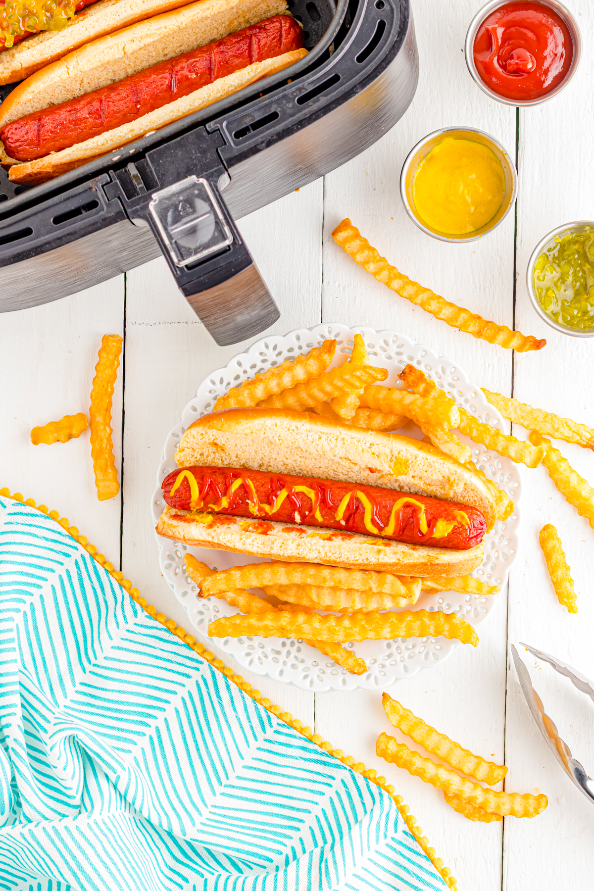 Air fryer hot dogs on table with fries and condiments.