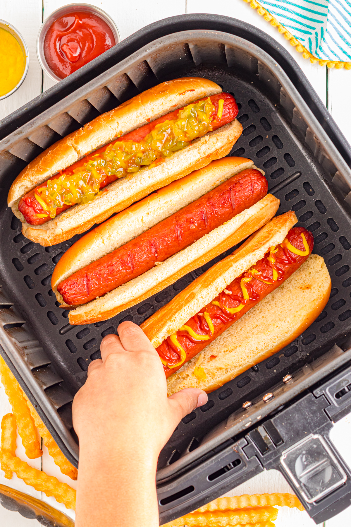 Child's hand grabbing a hot dog from the air fryer.