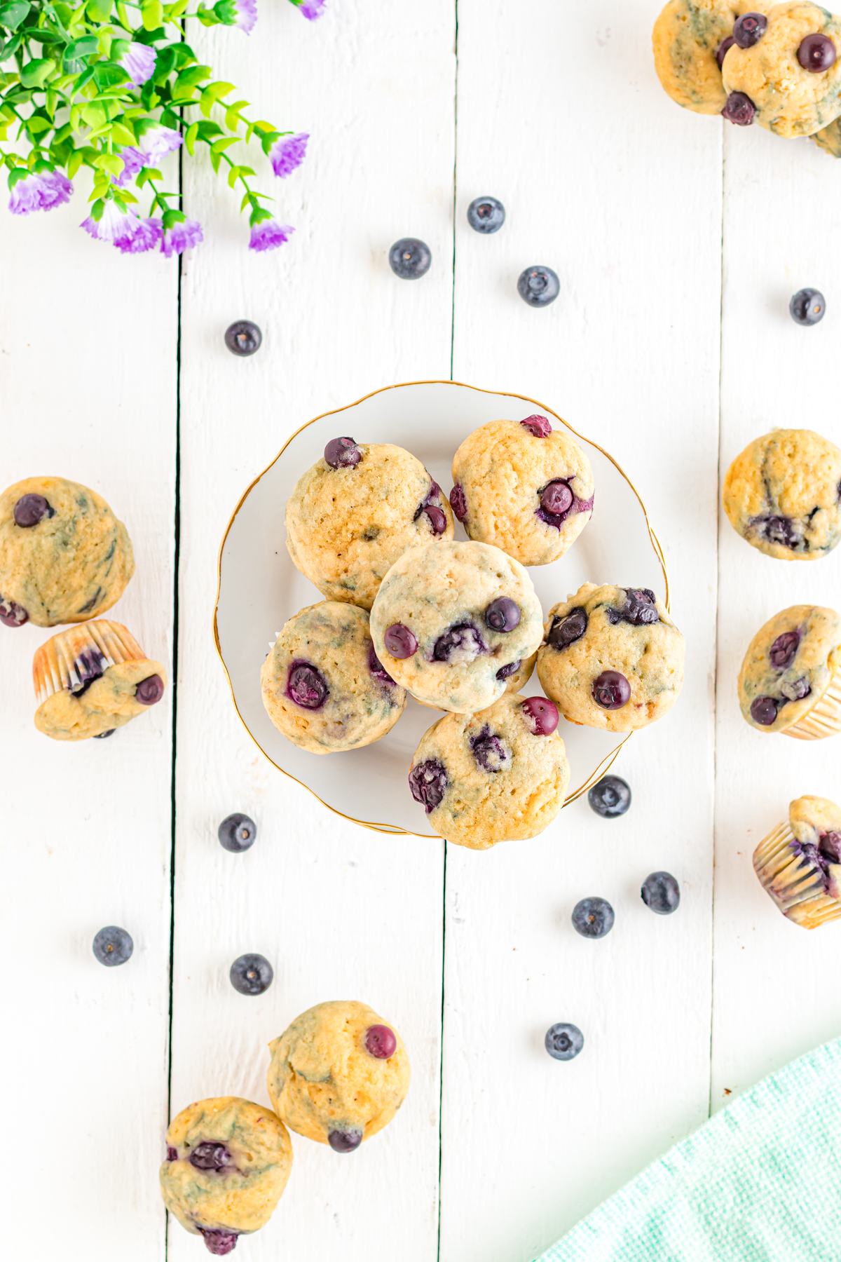 Mini blueberry muffins on table with flowers and fresh blueberries.