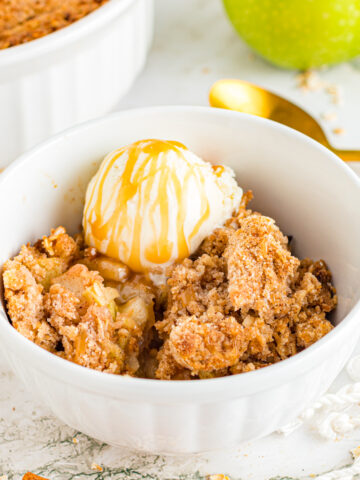 Apple crisp on table with ice cream and caramel sauce.