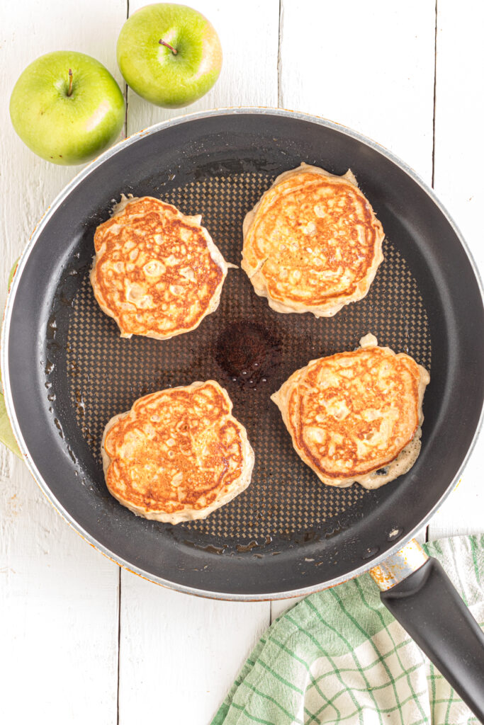 Flipped apple pancakes in frying pan.