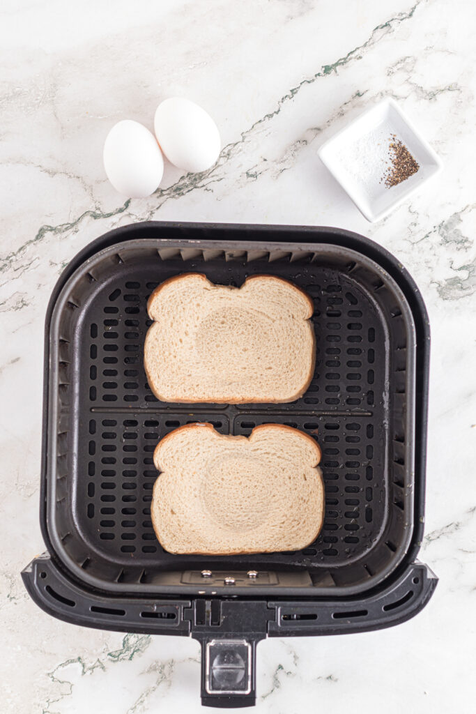 Bread slices in air fryer basket with indents for eggs.