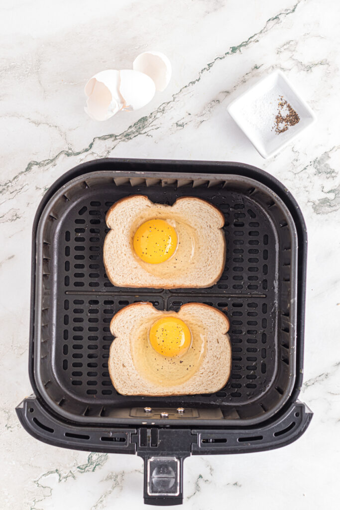 Eggs cracked in bread holes in air fryer basket.