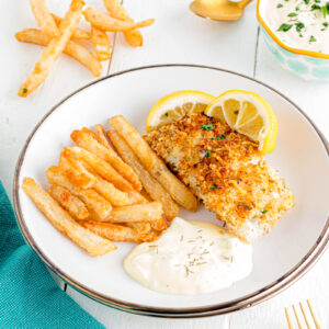 Panko crusted cod made in the air fryer on a plate with fries and tartar sauce.