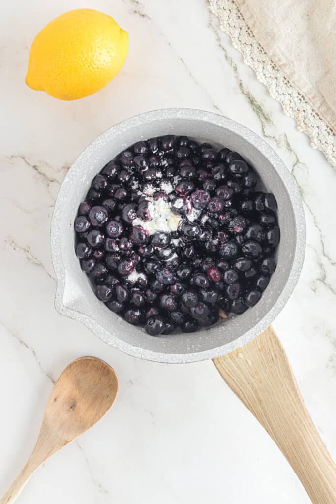 Adding blueberries and cornstarch and lemon juice to a saucepan.