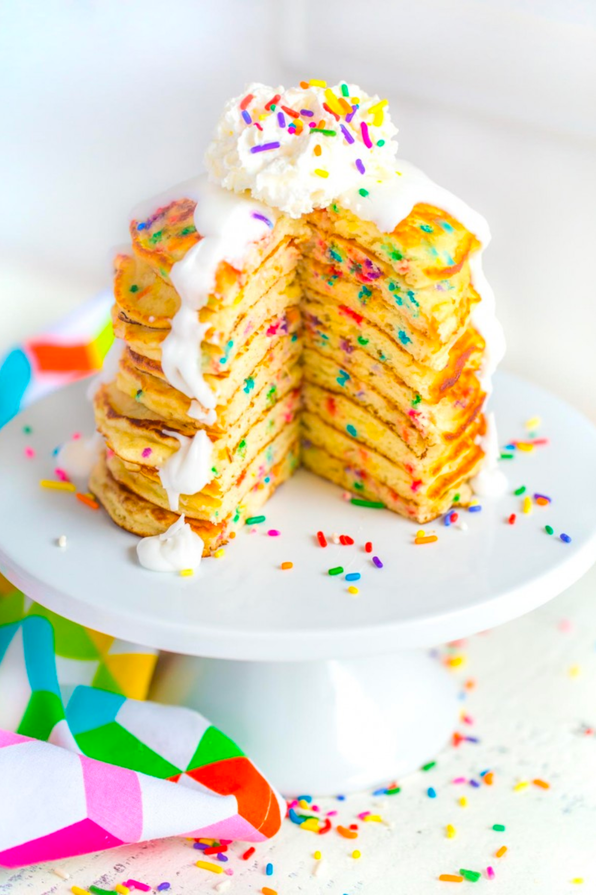 Stack of birthday cake pancakes on a cake stand.