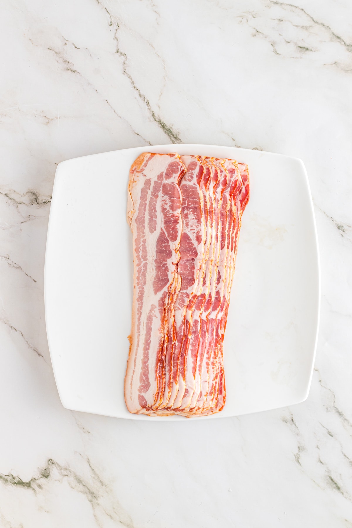 Raw bacon on a white plate.