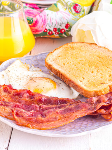 Bacon in a toaster oven on a plate with eggs and toast.