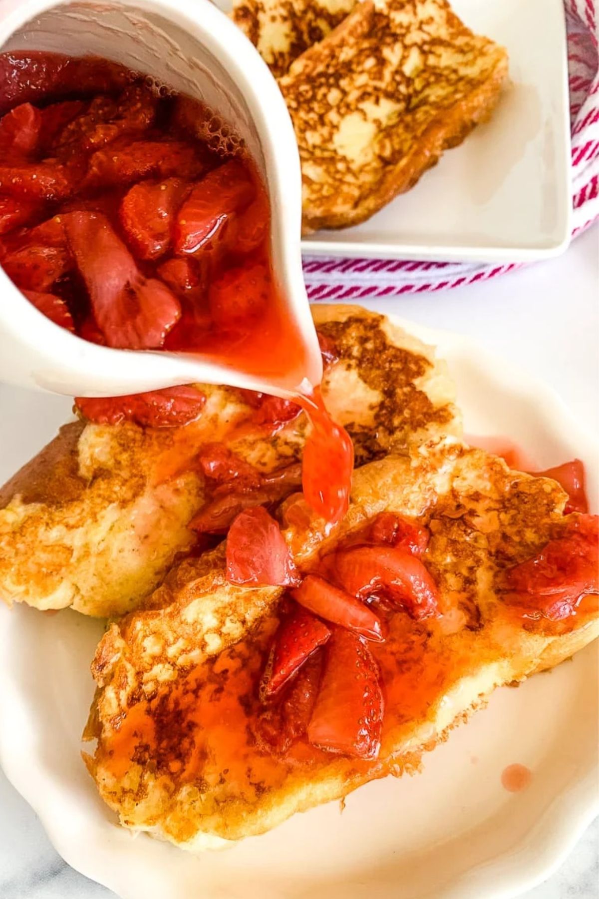 strawberry syrup being poured over french toast.