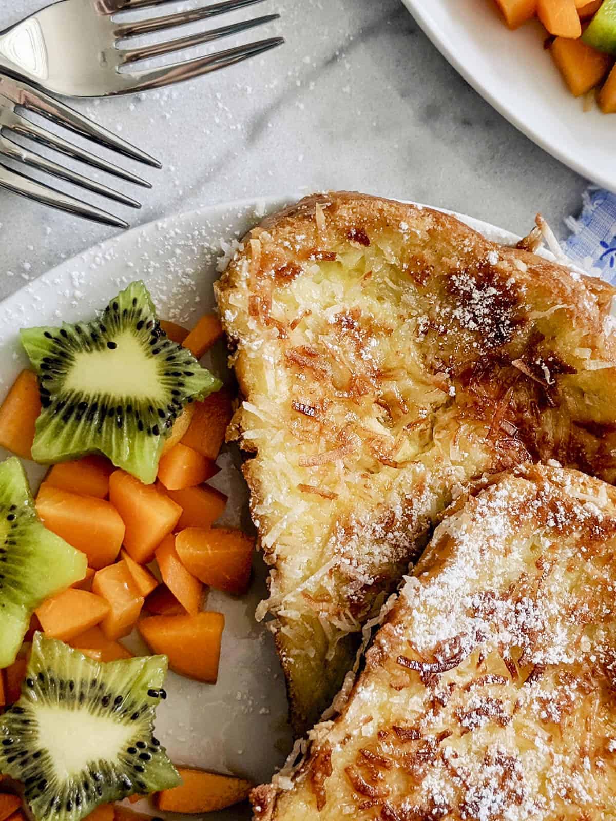 Coconut french toast on plate with kiwi and papaya.