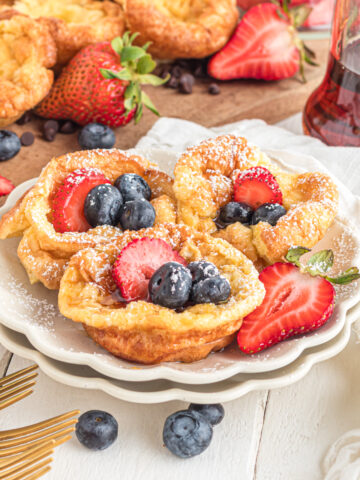 Mini Dutch babies on plate topped with berries and powdered sugar.