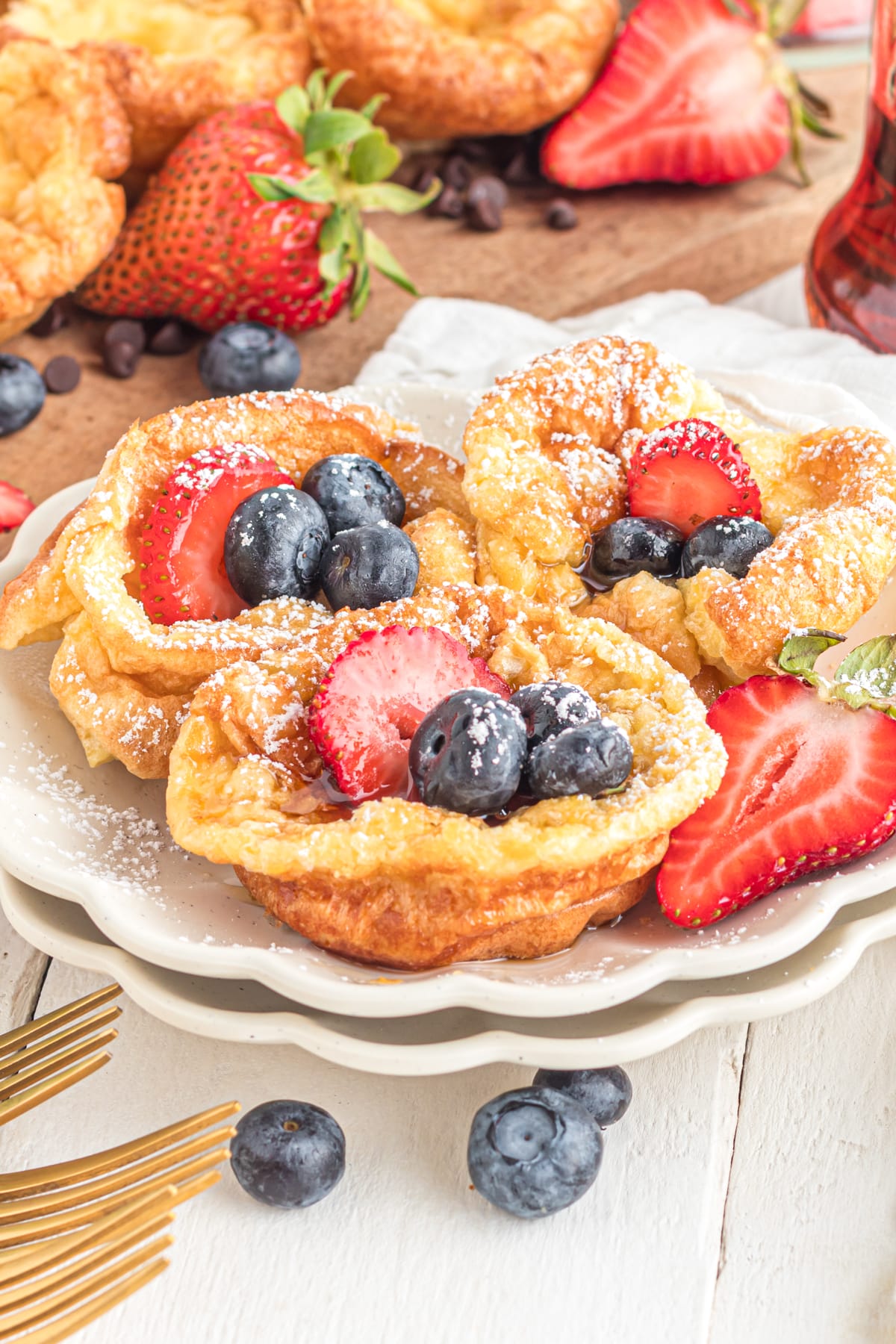 Mini dutch babies on plate topped with berries, syrup and powdered sugar.