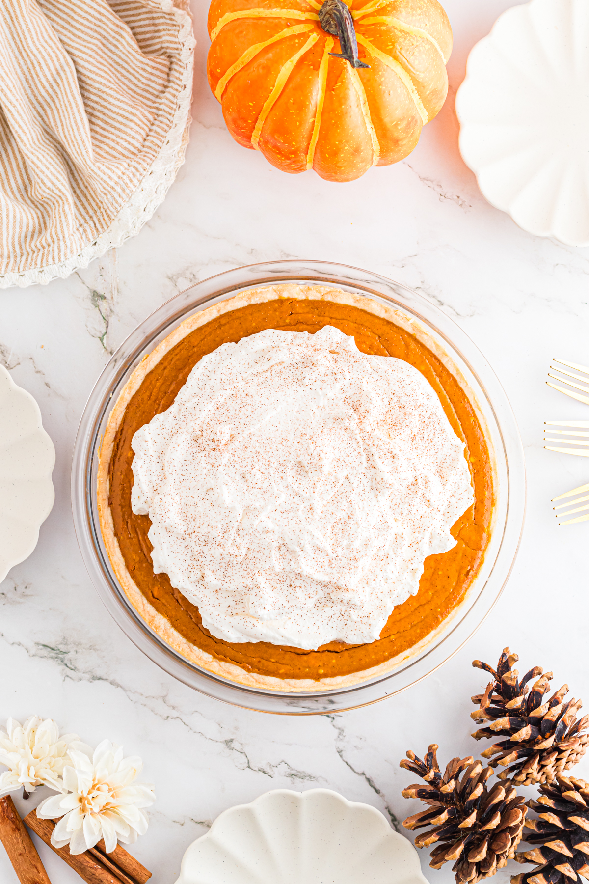 Pumpkin pie on table with pine cones and cinnamon sticks.